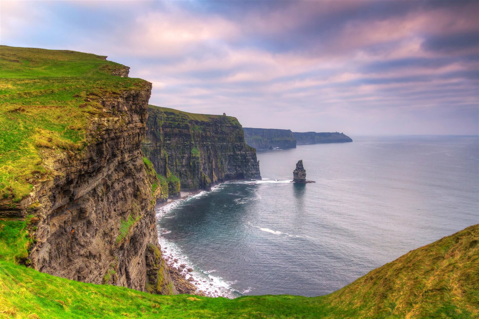 Green Atlantic cliffs and sea stacks beneath a pastel evening sky